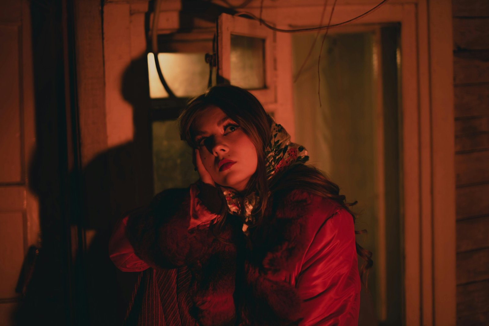 A woman in a red coat gazes thoughtfully in warm indoor lighting.
